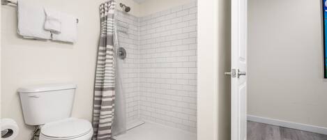 A bathroom with a toilet, a shower with a striped curtain, and a white tiled wall.