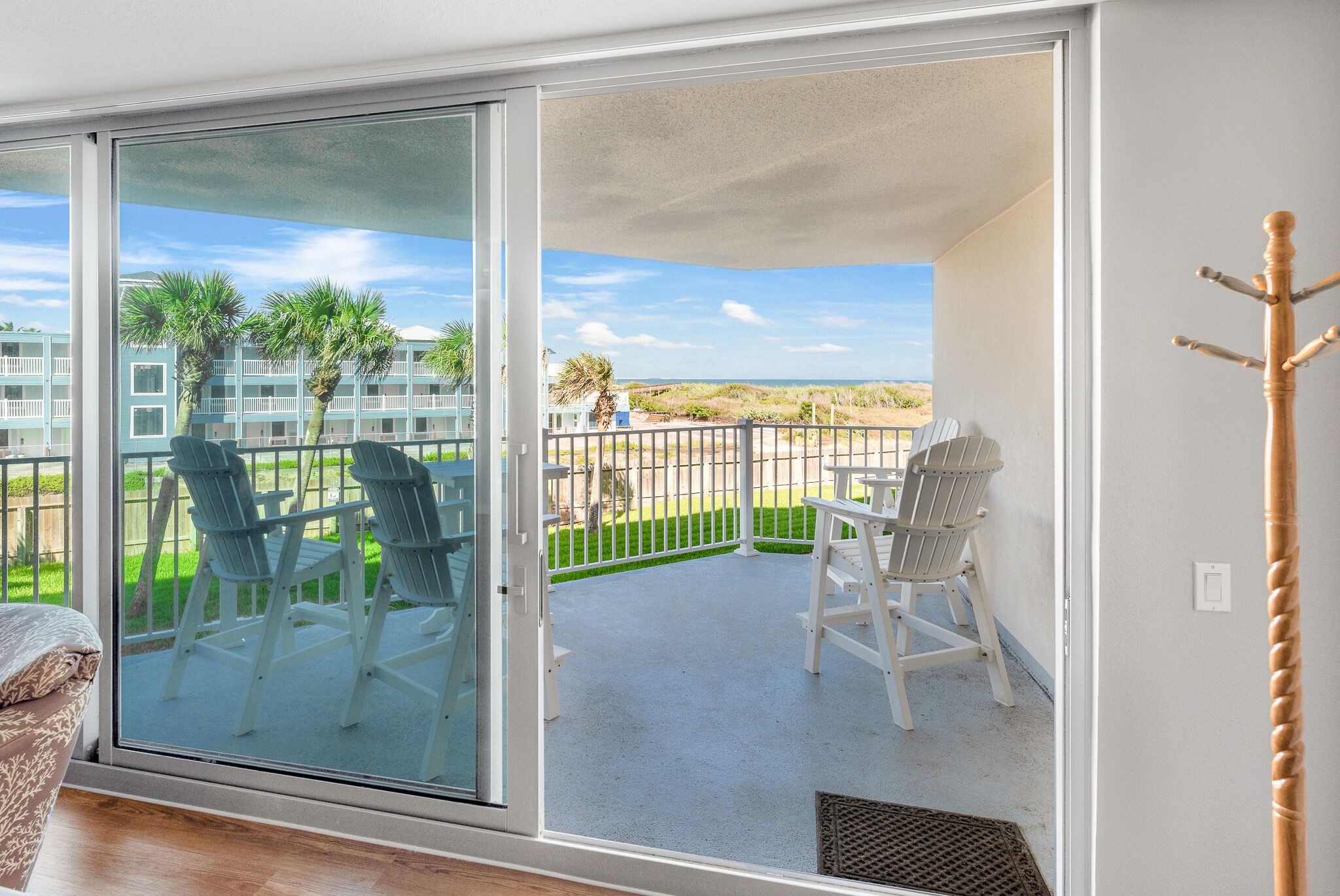A balcony with two chairs and a table, overlooking a beach and a building with a blue facade.