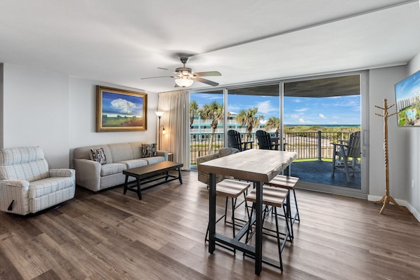 Relax in this stylish living room with a sofa set, coffee table, and dining table, plus a large balcony with a view of the surrounding landscape.