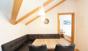 A room with a wooden ceiling, a dining table with four chairs, a black leather bench, and a wall clock.