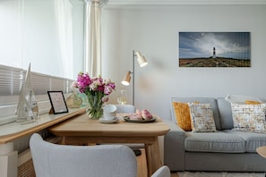 En moderne stue med et træspisebord, en grå sofa og et maleri af et fyrtårn.