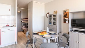 A compact kitchen with a dining area, including a table with chairs, a TV, and a cabinet with glass doors. - Beautiful apartment for 4 people with WIFI, TV, balcony and pets allowed (Mimizan)