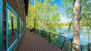 A wooden deck with a railing overlooking a lake, surrounded by trees.
