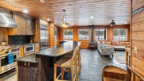 A spacious kitchen with wooden cabinets, a large island, and a fireplace. There is a seating area with a sofa and chairs.