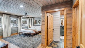 A bedroom with a bed, a bench, a ceiling fan, and a view of the outside.