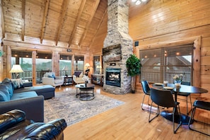 A spacious living room with a stone fireplace, wooden ceiling beams, and a cozy seating area with a sofa and chairs.