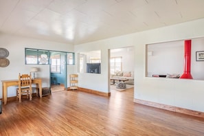 A spacious living area with wooden flooring, a dining table with chairs, a fireplace, and a red chimney.