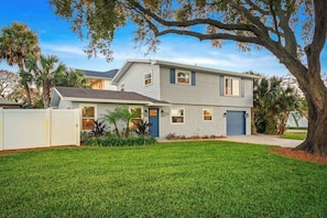 A two-story house with a front yard, a driveway, and a large tree.