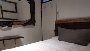 A bedroom with a bed, a wooden headboard, a bench, and a wall-mounted mirror. - Casa Zury Playa (QUEPOS)