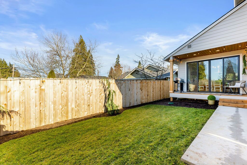 Una casa moderna con un patio in legno, un prato curato e un'ampia vetrata che si affaccia sul giardino.