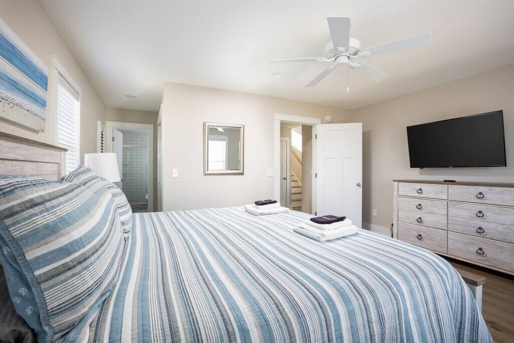A bedroom with a bed, a ceiling fan, a TV, and a dresser.
