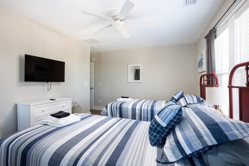 A bedroom with two beds, a ceiling fan, a TV, a bedside table, and a window with curtains.