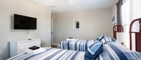 A bedroom with two beds, a ceiling fan, a TV, a bedside table, and a window with curtains.