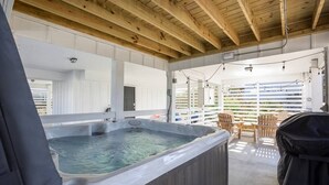 Een hottubgedeelte met houten balken, buitenmeubels en een overdekte barbecue.