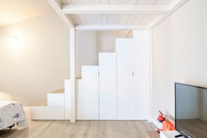 Une pièce avec une armoire blanche, un lit recouvert d’une couvre-lit à motifs floraux et un téléviseur.