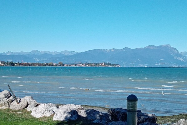 Une vue sur le lac, avec des montagnes en arrière-plan, une rive rocheuse et un ciel dégagé.