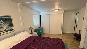 Een slaapkamer met een bed, een dressoir, een schilderij en een kast.