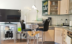 Una cocina moderna con comedor, que incluye un televisor, taburetes de bar y una cafetera.