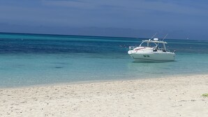Ein Boot vor Anker in der Nähe eines Sandstrandes mit klarem türkisblauem Wasser und wolkenlosem Himmel.