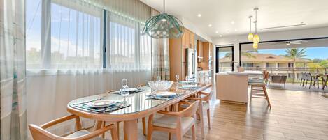 A modern dining area with a glass table, wooden chairs, and a view of the cityscape through large windows.