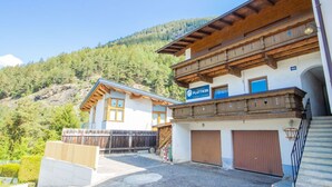 A two-story building with a wooden facade, a sign for 'Plattner', and a view of a forested hillside. - Beautiful  villa for 5 people with WIFI, TV and terrace (Oetz)