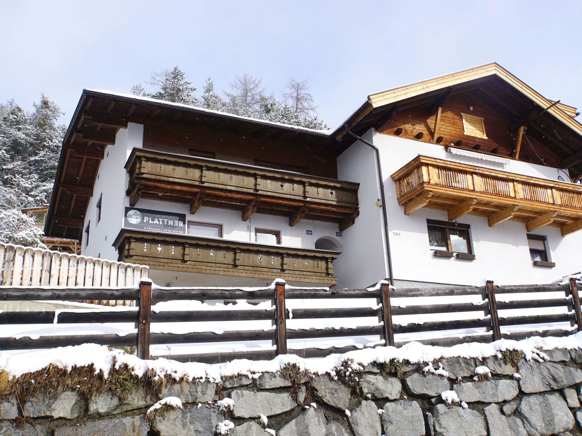 A traditional alpine building with wooden balconies and a stone wall in front.