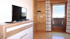 A wooden interior with a flat-screen TV on a wooden desk, a sliding door with a view, and a small shelf with decorative items. - Beautiful  villa for 5 people with WIFI, TV and terrace (Oetz)