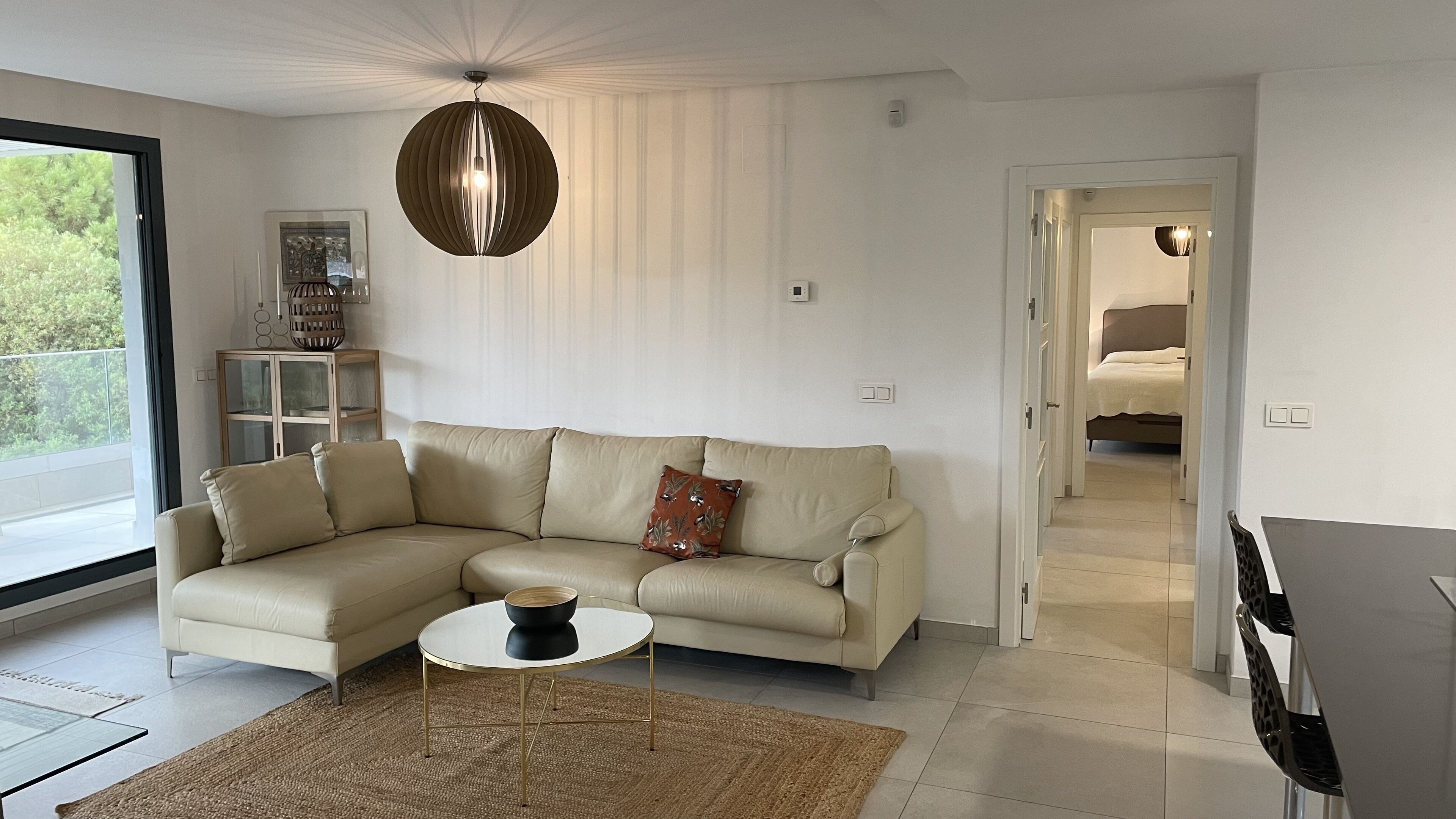 Een moderne woonkamer met een beige modulaire bank, een ronde salontafel en een hangende pendantlamp.
