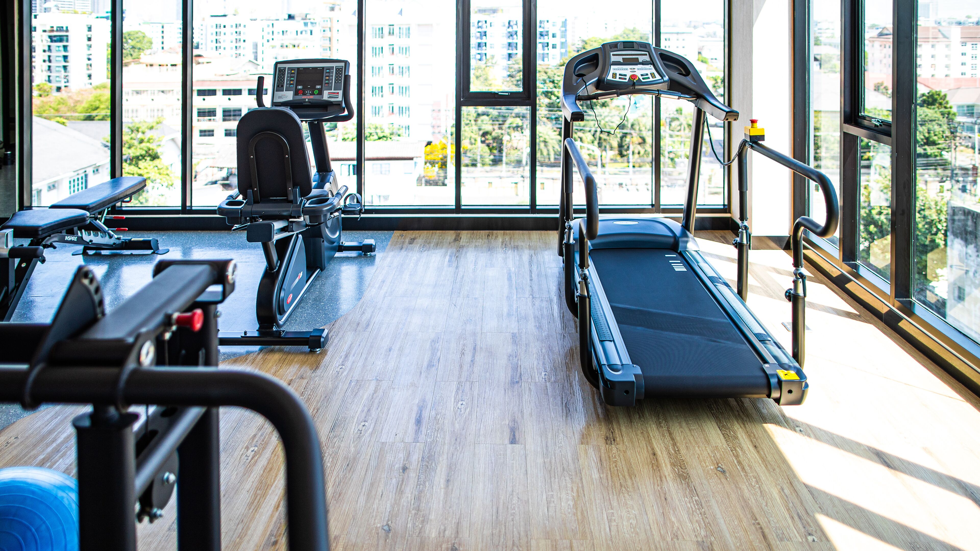 Une salle de sport équipée de matériel d’exercice, dotée de grandes fenêtres et offrant une vue sur les bâtiments.