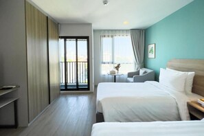A hotel room with two beds, a balcony, a small table with a vase, and a view of the city.