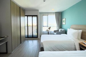 Habitación de hotel con dos camas, un balcón, una mesita con un florero y vistas a la ciudad.