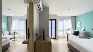A modern hotel room with a large bed, a desk with a computer, a sofa, and a balcony with a view.