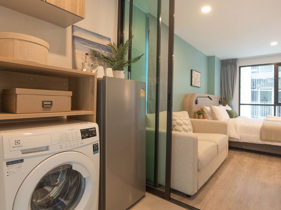 Un apartamento moderno con lavadora, refrigerador, sofá y puerta corrediza de vidrio que da a un balcón.