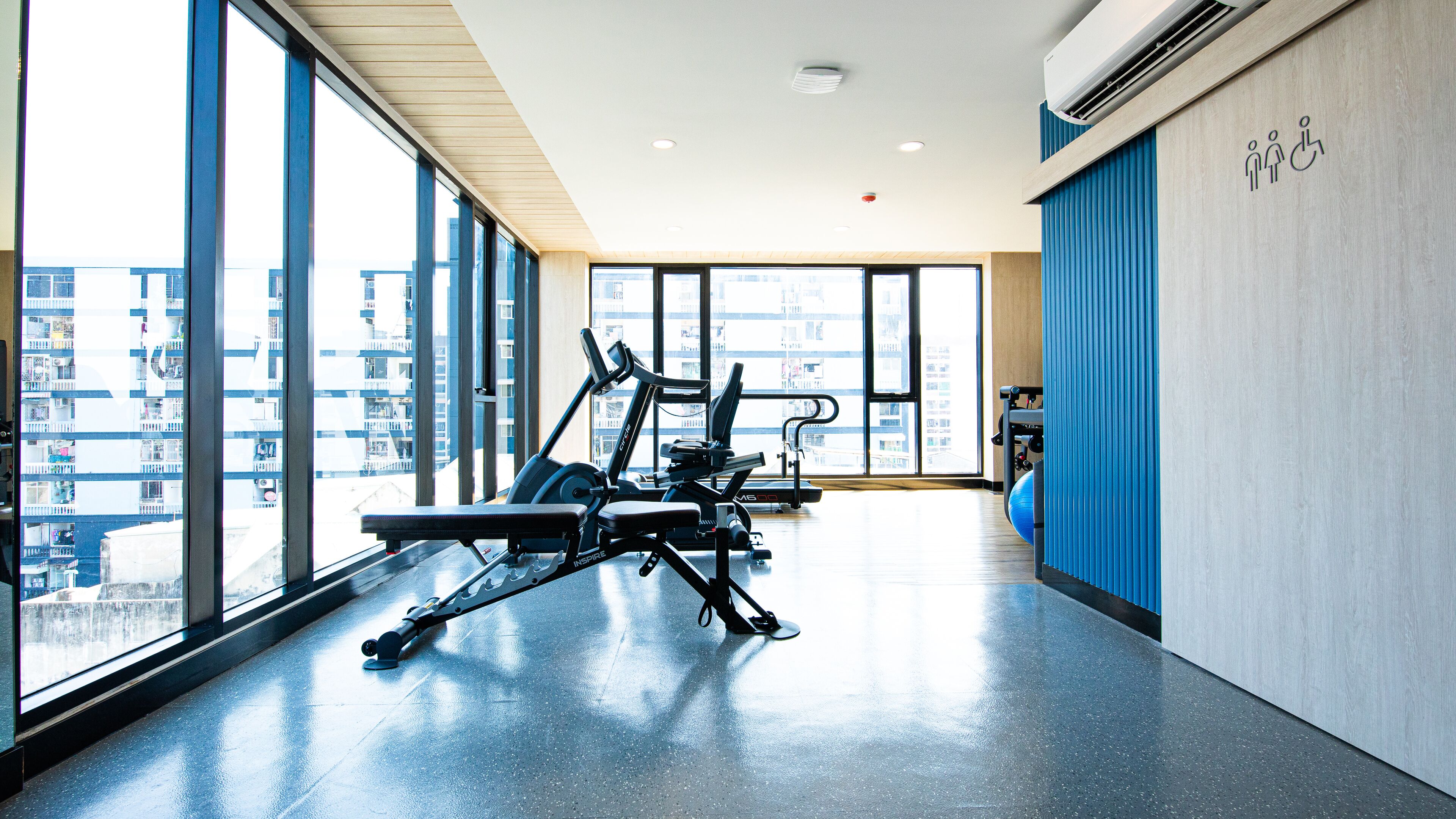Un gimnasio con equipo de ejercicio, ventanas amplias y vistas a un paisaje urbano.