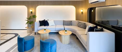 Una sala moderna con un sofá blanco, otomanas azules y mesas redondas de madera.