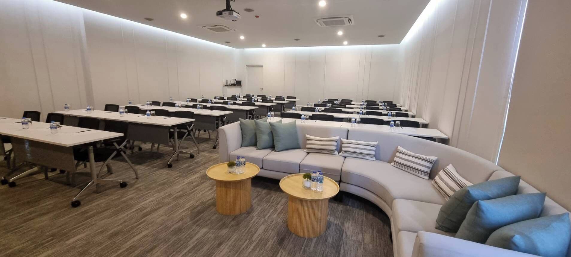 A conference room with multiple tables and chairs, a sofa, and two round tables with water bottles.