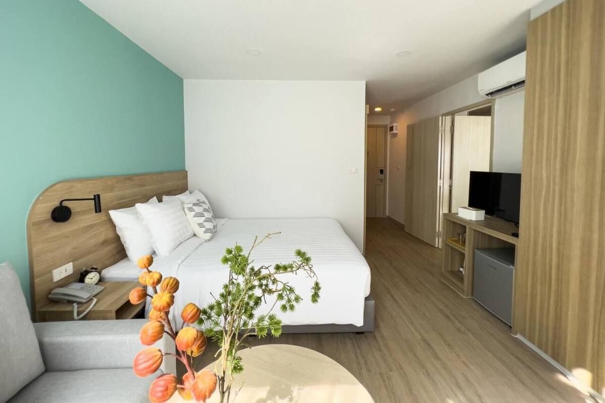 Una habitación de hotel moderna con una cama bien hecha, una mesita de noche con lámpara, un escritorio pequeño con silla, televisión y un armario.