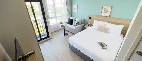Une chambre d’hôtel moderne avec un grand lit, un canapé, une petite table et une vue sur l’extérieur.