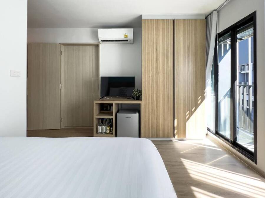 Una habitación de hotel moderna con una cama grande, un escritorio con computadora, un mini refrigerador y un armario.