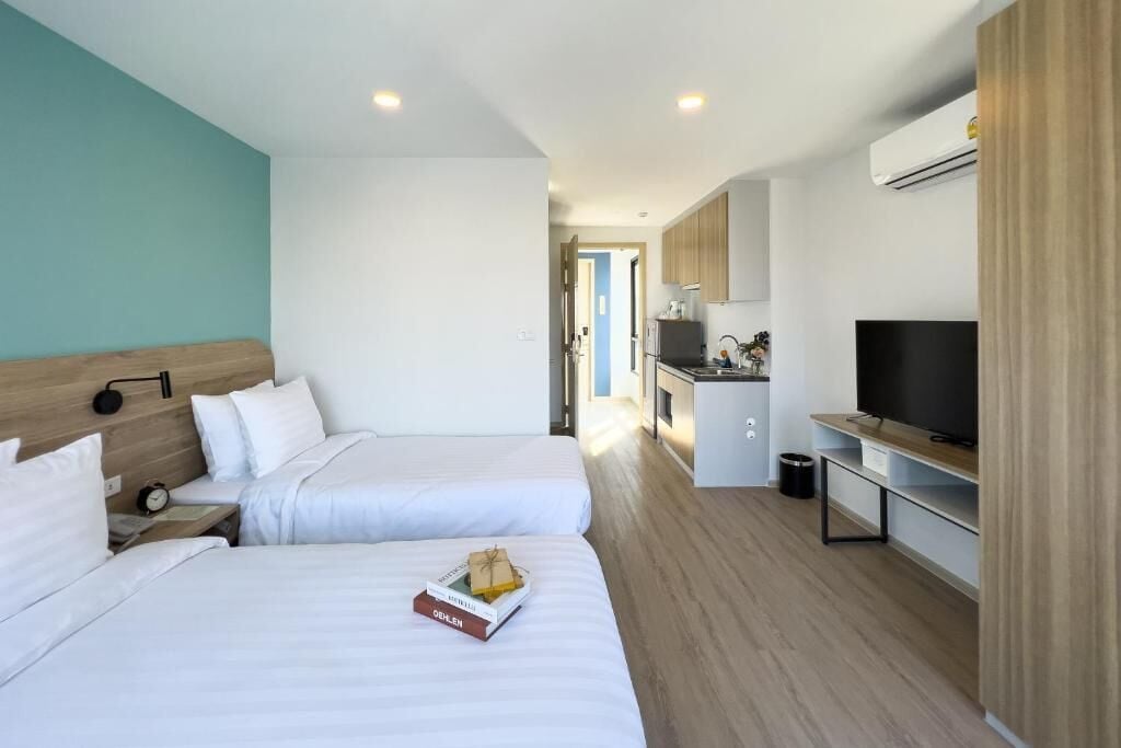 A hotel room with two beds, a TV, a kitchenette, and a bathroom visible through an open door.