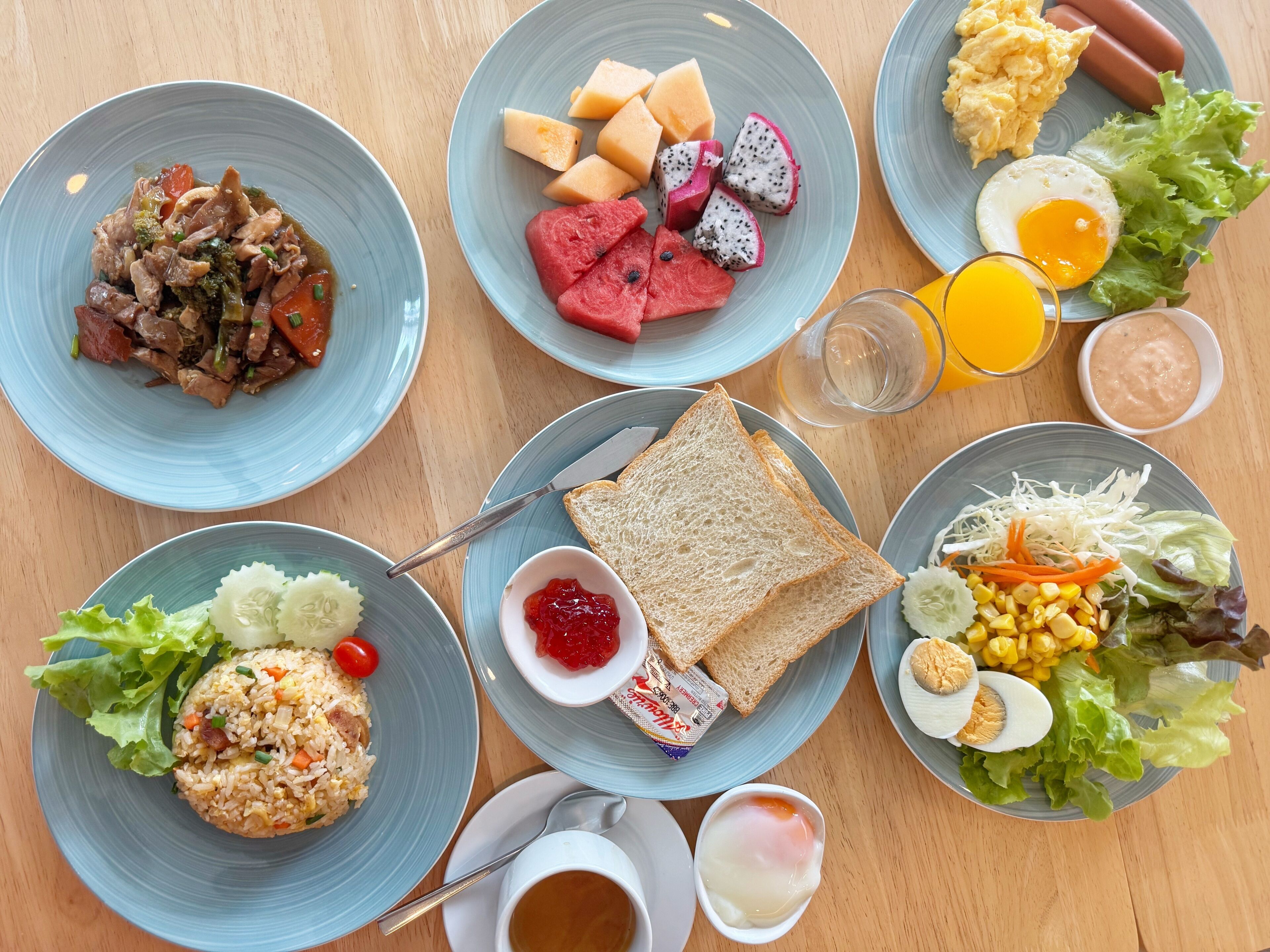 Una mesa con diversos platos para el desayuno, como arroz frito, huevos y frutas frescas.
