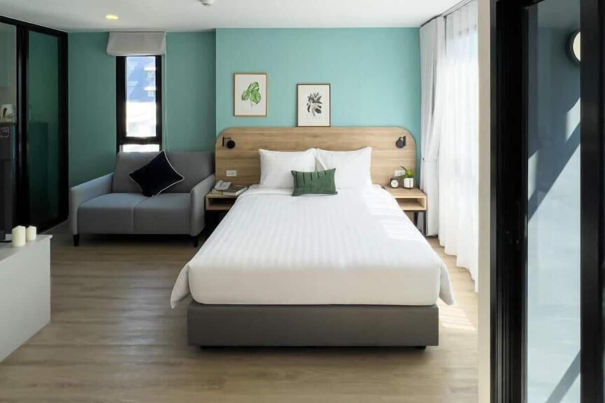 Una habitación de hotel moderna con una cama grande, un pequeño sofá, una mesita de noche y una ventana con cortinas.