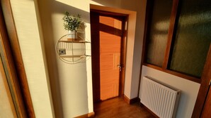 A hallway with a wooden door, a radiator, and a wall-mounted shelf with a plant. - Captivating 1-Bed Apartment in Edinburgh (Edinburgh)