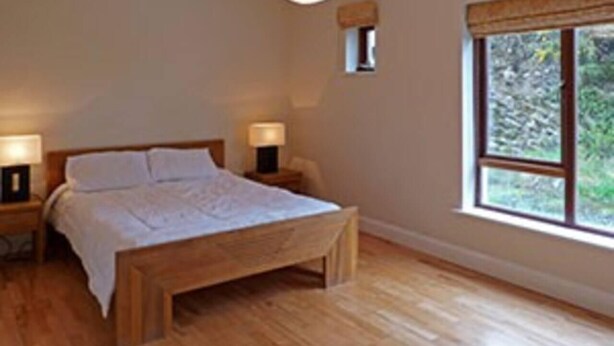 Een slaapkamer met een houten bed, twee nachtkastjes en een raam met uitzicht op groen.