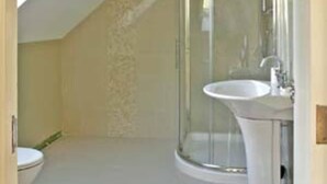 Een kleine, afgesloten doucheruimte met een glazen deur, een witte wastafel en een toilet.