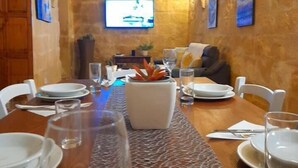 Un comedor con una larga mesa dispuesta para una comida, un televisor montado en la pared y una pared de piedra con arcos.