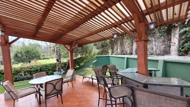 Un espace extérieur aménagé en terrasse, avec une pergola en bois, une table ronde entourée de chaises et un comptoir de bar.