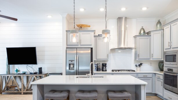 A modern kitchen with white cabinetry, a central island with bar stools, stainless steel appliances, and pendant lighting. - Cozy 3bed townhome close to beach/step from Hub (Rosemary Beach)