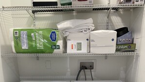 A laundry area with two white front-loading washing machines and shelves above containing various laundry supplies.