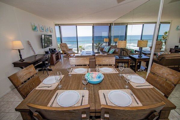 A dining area with a view of the ocean, featuring a wooden table set for four, chairs, and a sofa with a view.